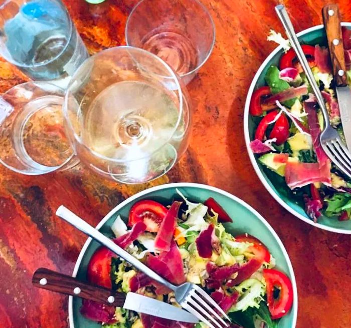 Two plates of vibrant salad placed on a wooden table, accompanied by glasses of wine and a lovely vase of flowers.