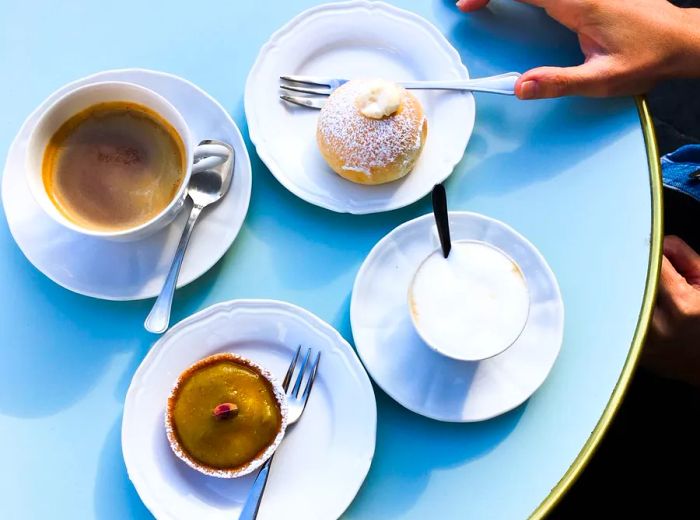 An overhead view of a vibrant blue table adorned with plates of pastries and coffee drinks.