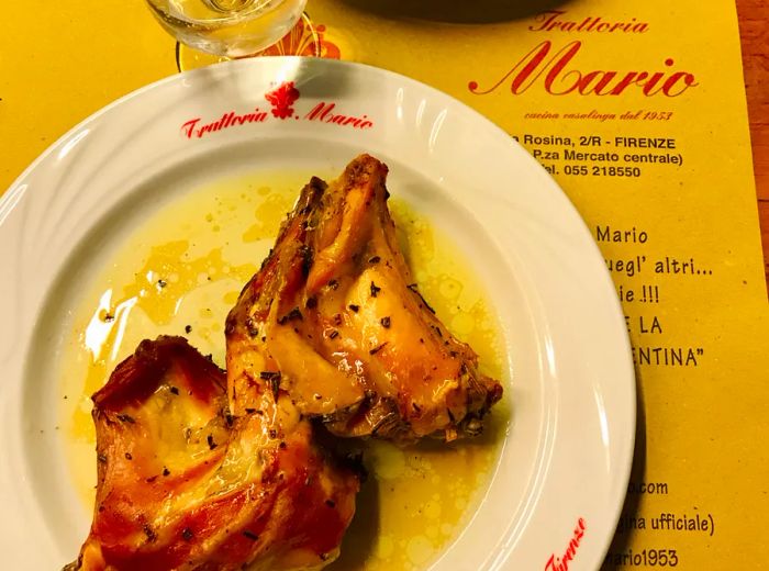 A plate featuring two cuts of rabbit, accompanied by a menu and a glass of wine.