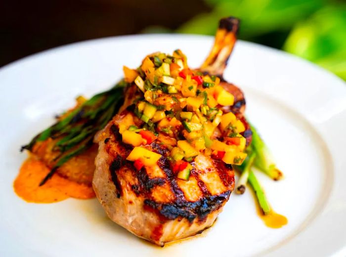 A sizable pork chop elegantly positioned on a vibrant mix of chopped vegetables, framed by a bright outdoor setting.