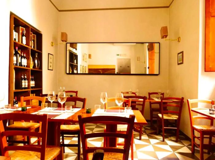 An interior shot of the restaurant featuring checkerboard flooring, wooden tables set for lunch, a long mirror adorning the back wall, and wine shelves on one side.