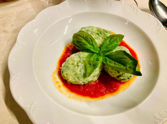 A trio of large, green gnudi nestled in tomato sauce, garnished with herbs.