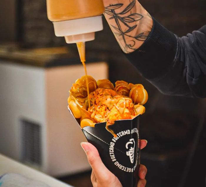 A staff member drizzles caramel from a squeeze bottle onto a fluffy waffle cone filled with ice cream.