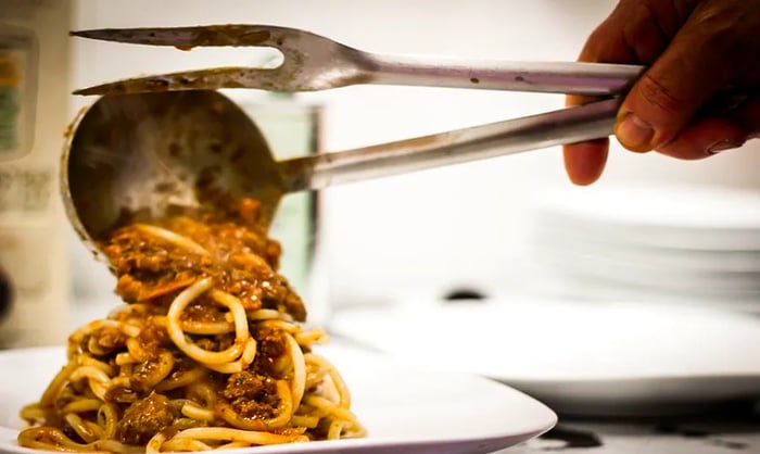 A chef’s hands skillfully serve a generous portion of meat-filled pasta onto a plate.