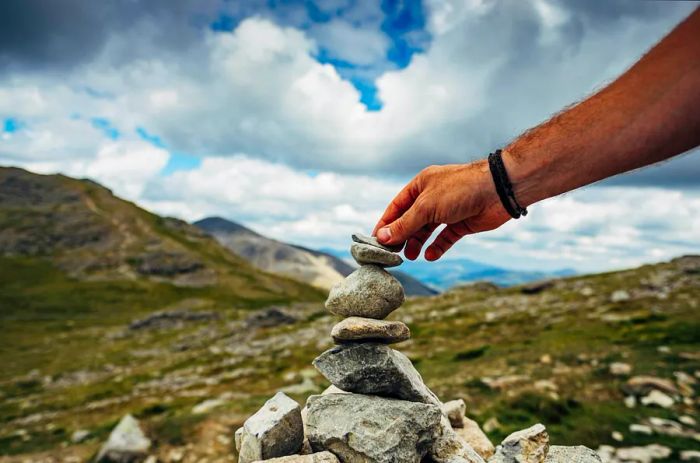 A hand placing a stone atop a cairn.