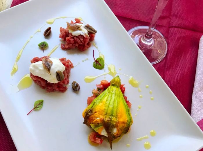 A plate featuring a stuffed zucchini flower alongside small mounds of tartare.