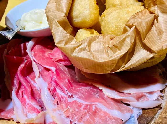 A paper bag filled with fried dough, accompanied by strips of meat and a small dish of cheese.