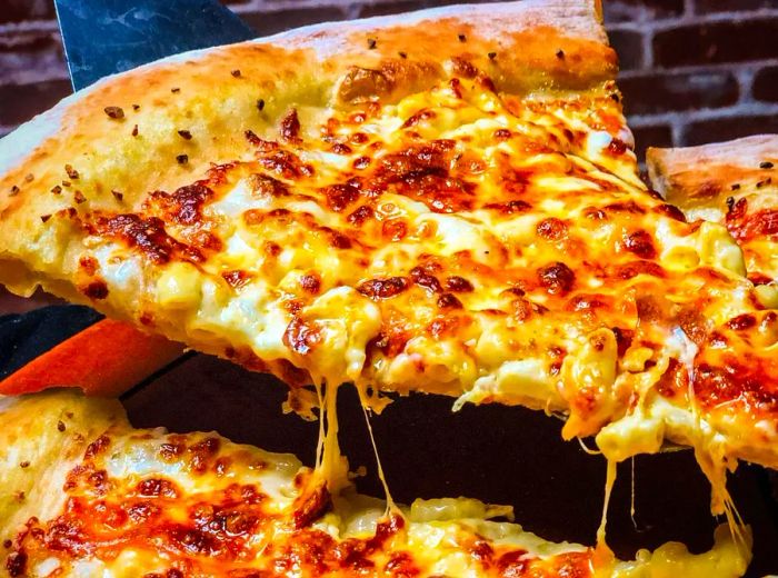 A slice of mac and cheese pizza being pulled from the pie, with cheese stretching down in gooey strands.