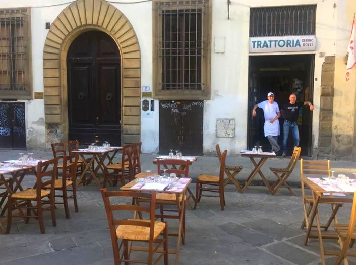 Outdoor seating in front of a restaurant, with two men casually leaning in the doorway.