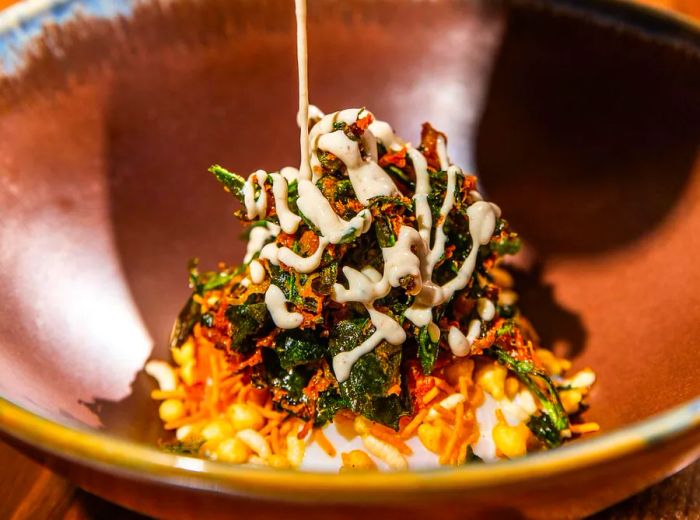 A serving of chaat topped with crispy spinach, elegantly drizzled with white sauce.