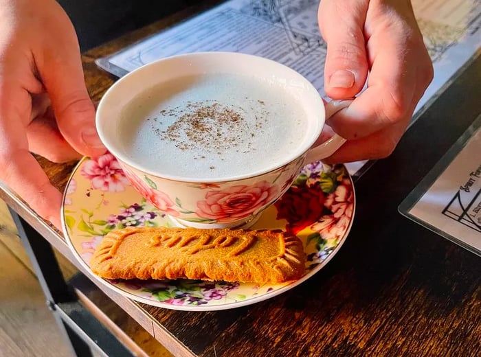 A server presents a rich cocktail in an elegant teacup, accompanied by a small rainbow platter and a cookie.