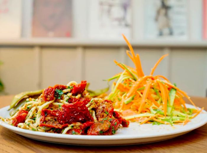 A dish featuring a division of red sauce zucchini noodles and a shaved salad, elegantly presented on a table with decorative wallpaper in the background.