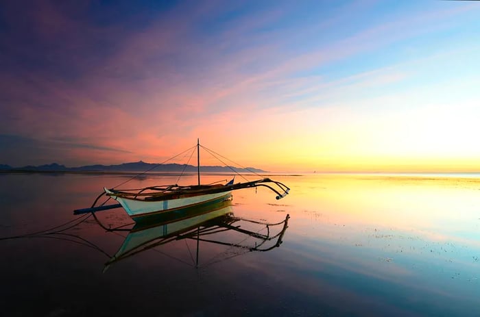 An outrigger boat sails into the sunset on Bohol Island, Philippines