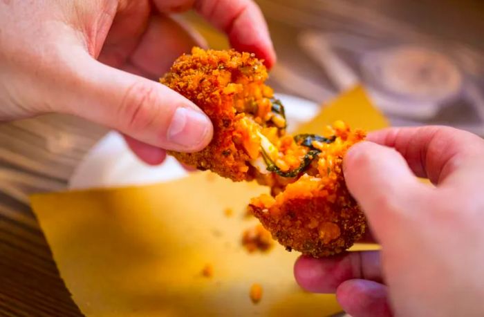 A cheesy rice ball is pulled apart by hand.