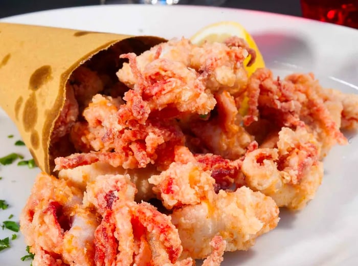 Crispy fried calamari tumbling out of a paper cone onto a plate.