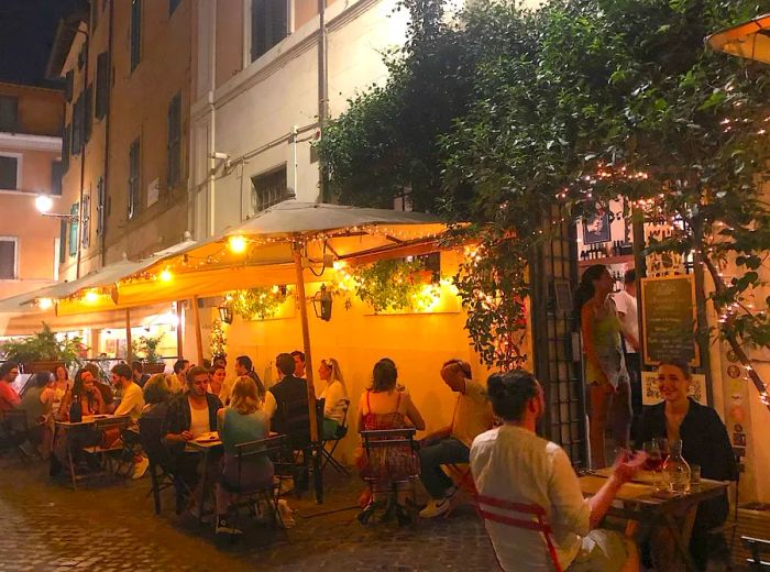 Guests enjoy dinner at outdoor tables adorned with umbrellas and string lights, set against the backdrop of a restaurant facade.