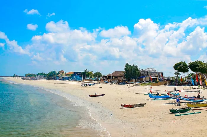 Colorful fishing boats are lined up along a sandy beach, with simple structures in the background.