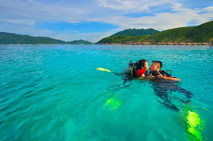 A couple of scuba divers share a kiss at the surface of the water in a tropical paradise.