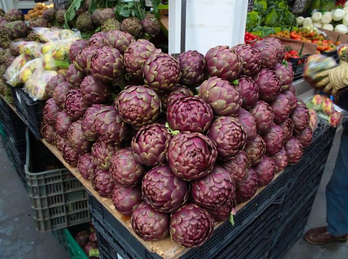 A pile of vibrant purple artichokes displayed at a farmer’s market.