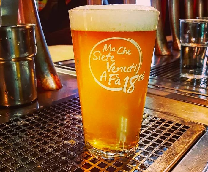 A branded pint glass filled to the brim with beer on a bar counter.