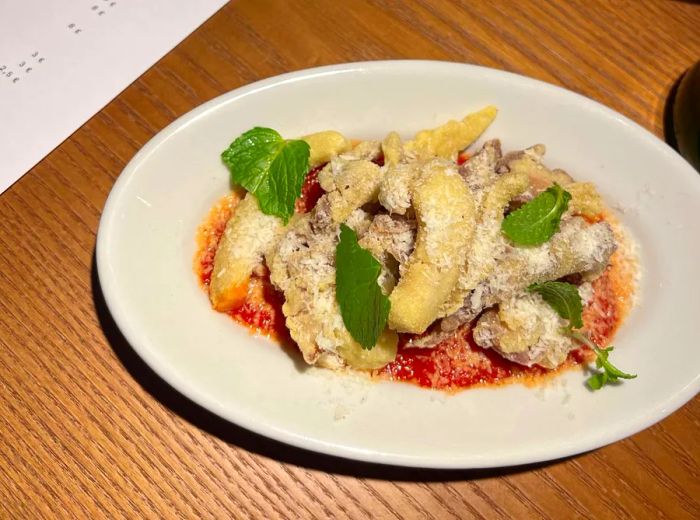 Fried tripe slices topped with grated cheese, resting in a pool of tomato sauce.