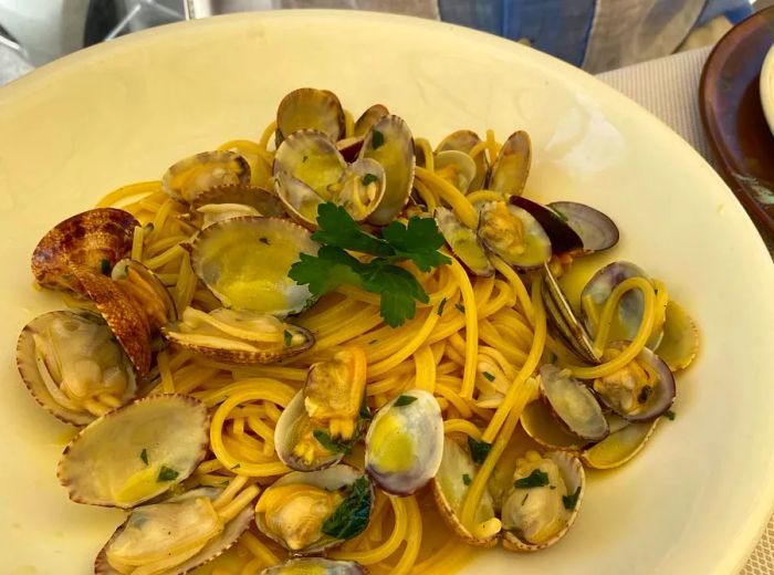 A shallow plate of spaghetti with clams, with a diner seated in the background.