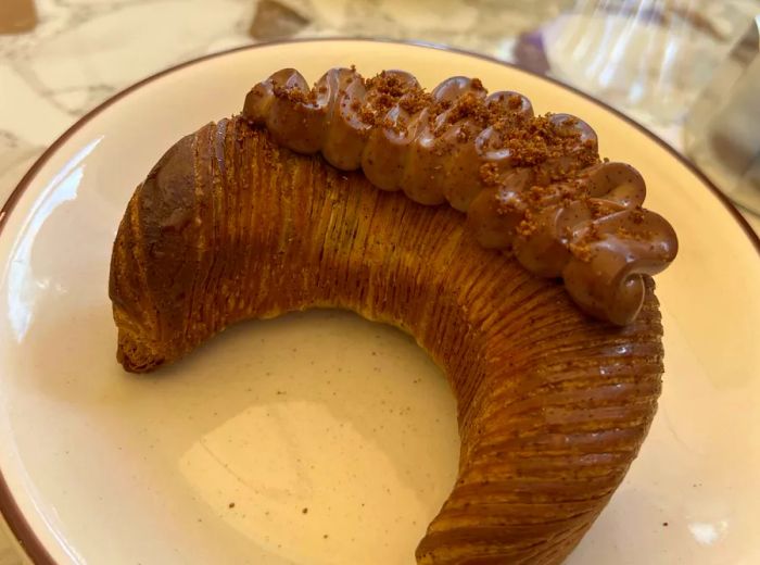 A croissant-inspired pastry adorned with swirls of brown cream.