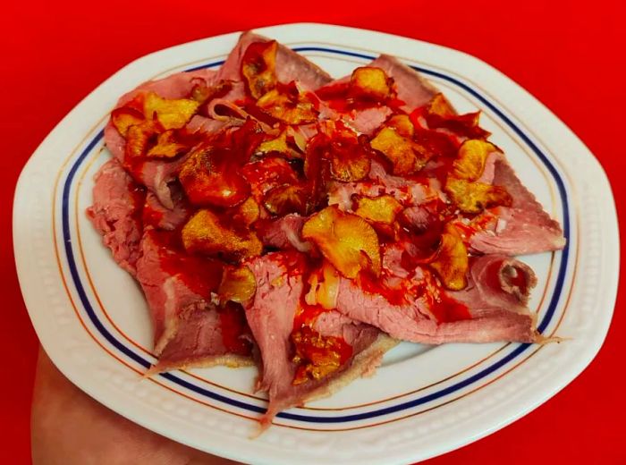 Tender sliced meats adorned with sauce and accompanied by sliced tubers.