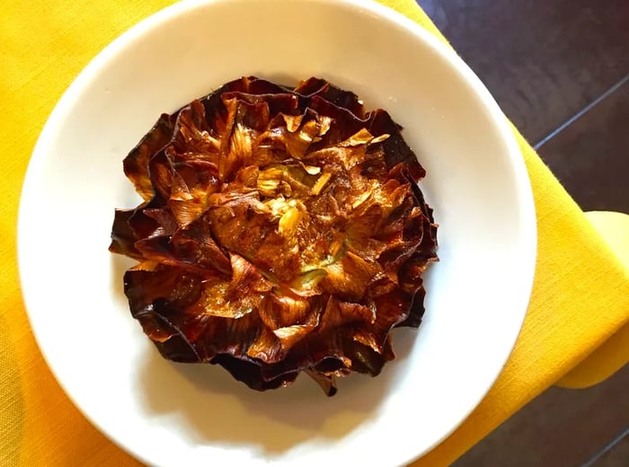 A sizable fried artichoke rests on a plate at the edge of a table.