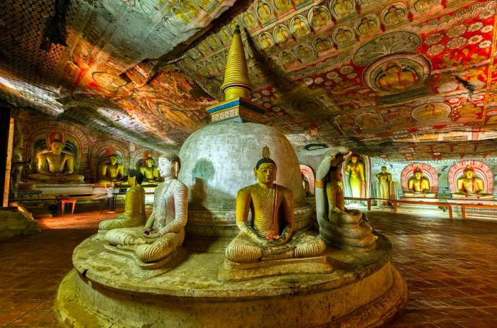 Buddha statues and vibrant religious artwork within the dimly lit caves of Dambulla