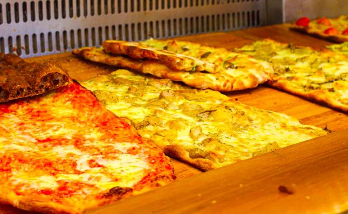 A display case filled with pizza slabs topped with various ingredients.