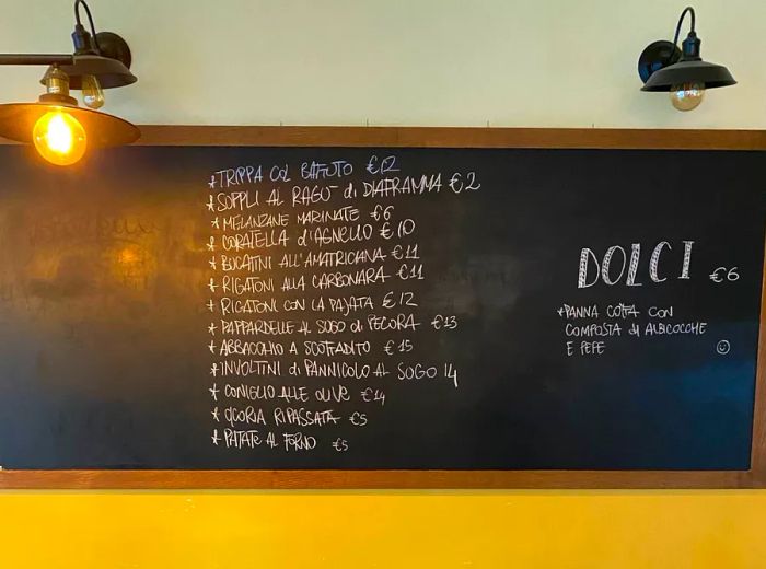 A chalkboard menu displayed on the wall of a dining area, adorned with pendant lights, a checkered floor, and a table set for two ready for dinner.