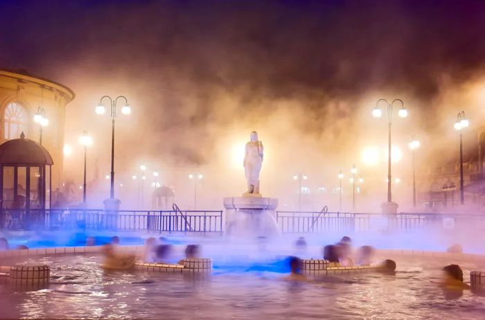 Visitors enjoying the Szechenyi Spa at night, with a statue in the foreground