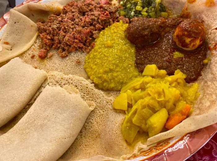 A selection of stews served on injera, accompanied by rolled flatbread on the side.