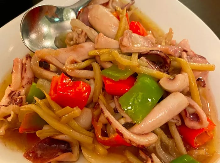 A heart-shaped presentation of squid accompanied by vegetables in a light sauce.