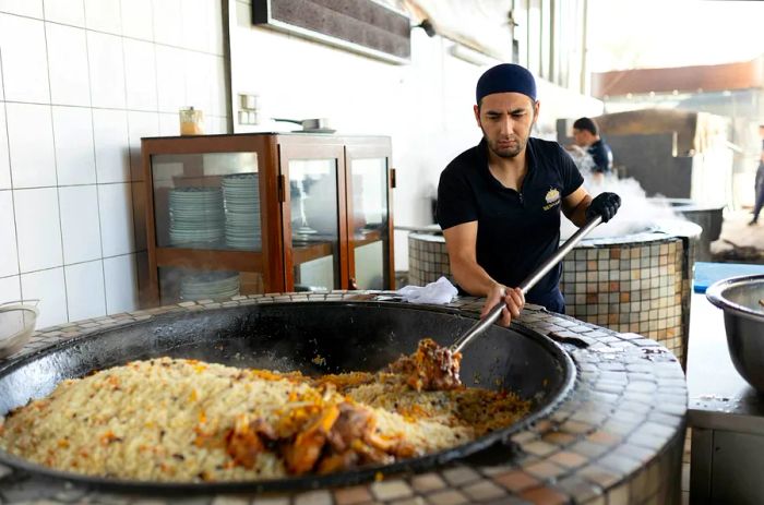 A chef skillfully prepares traditional Uzbek pilaf in a large cauldron.