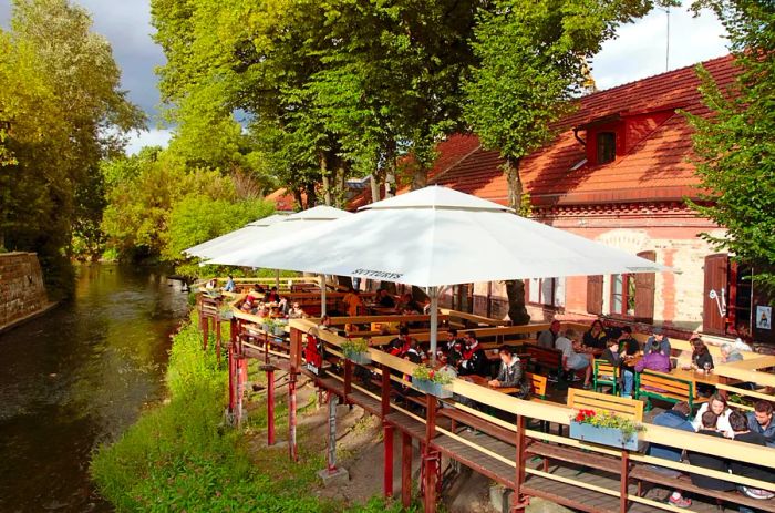 People enjoying a leisurely moment on a café terrace by the River Vilnele in the Užupis neighborhood, Vilnius, Lithuania.