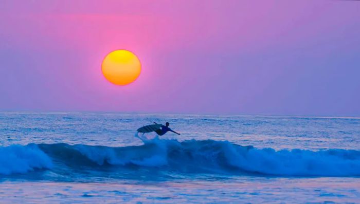 A surfer rides the waves against the backdrop of a sunset at Playa Carmen in Costa Rica.