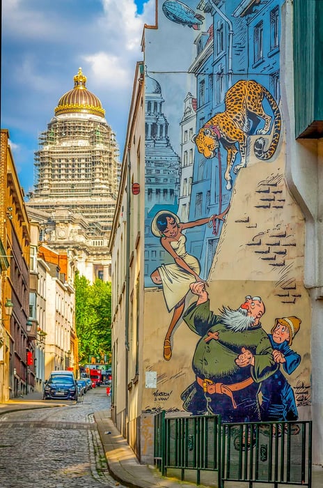 A vibrant mural depicting a comic book scene adorns the entire wall of a traditional house along a narrow cobbled street in Brussels.