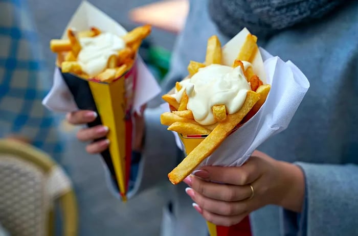 A woman enjoys two traditional paper cones filled with fries, generously topped with mayonnaise.