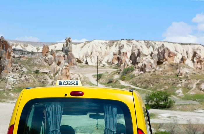 A yellow taxi marked 'taksi' drives through a rugged landscape in Türkiye