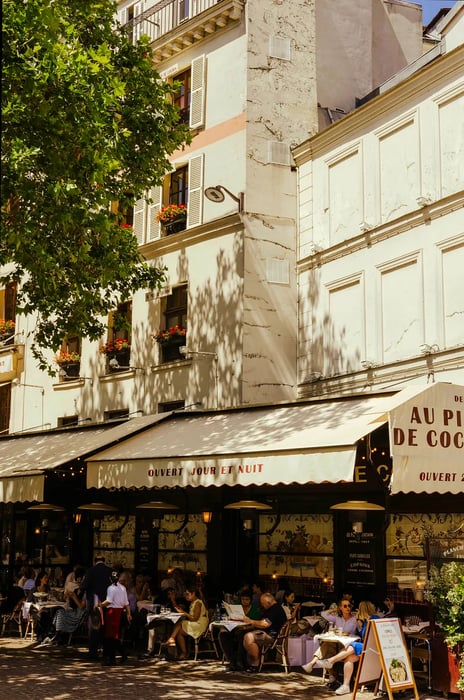 Patrons relax at a sidewalk cafe beneath the awning of the iconic Parisian restaurant Au Pied de Cochon.