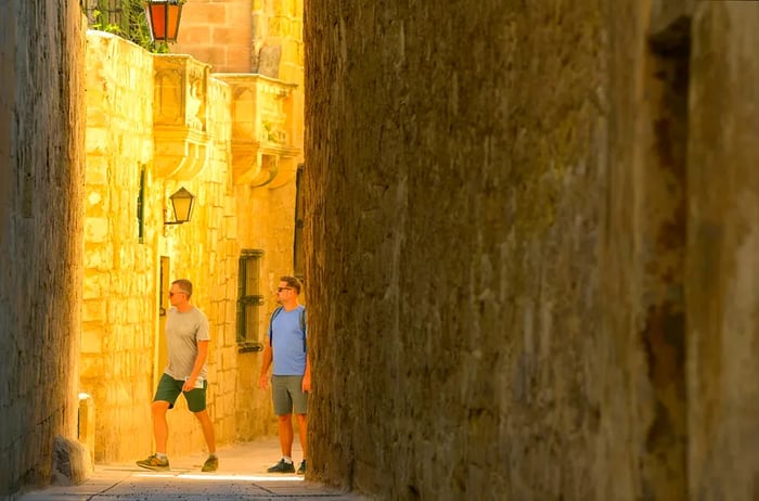 Two men stroll through a partially shaded alley in Mdina, Malta.