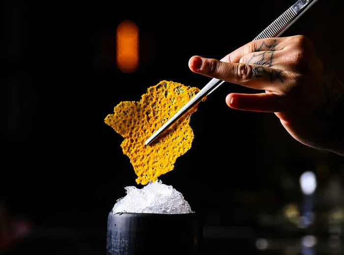 A bartender finishes a drink with a large, honeycomb-inspired garnish.