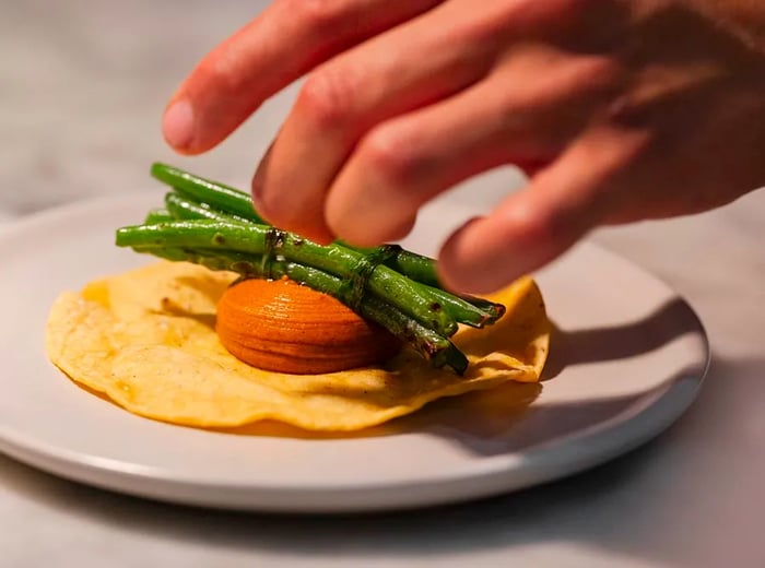 A chef artfully arranges scorch-marked green beans atop a tortilla with puree.