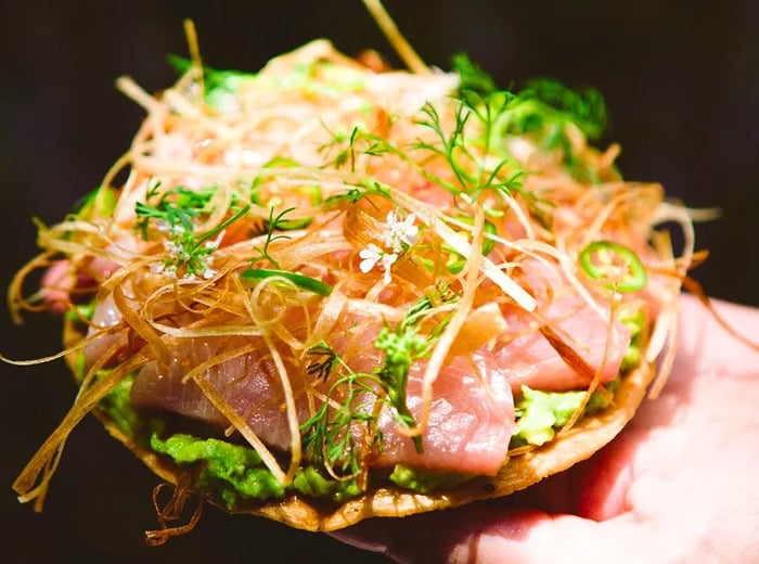 A hand holds a tostada brimming with fish and toppings.