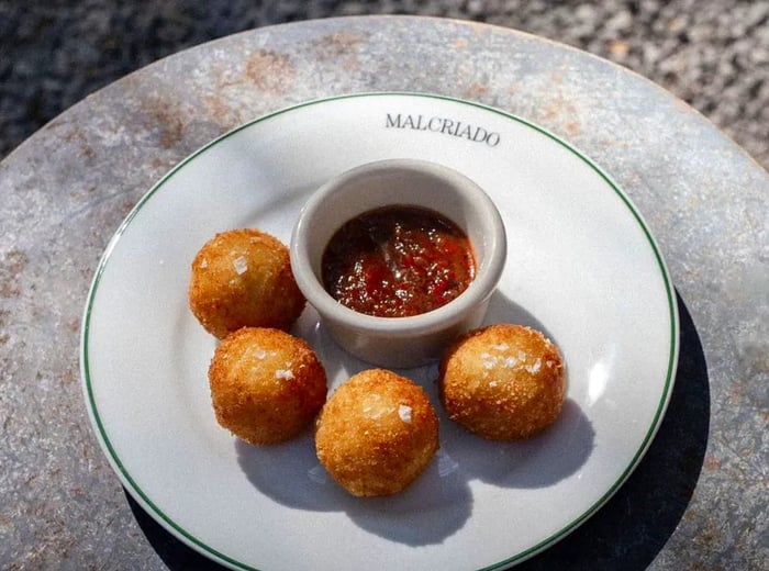 Four arancini arranged around a small dish of dipping sauce.