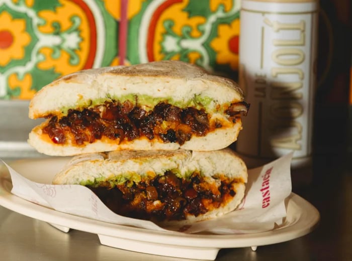 A torta, cut in half and stacked, rests on a counter next to a squeeze bottle of sauce and beautifully decorated wall tiles.