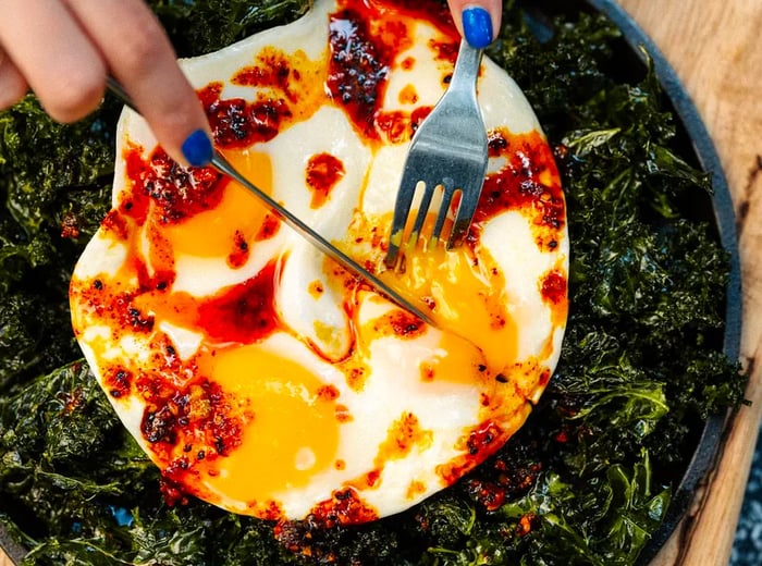 A diner slices into fried eggs adorned with ribbons of red salsa.