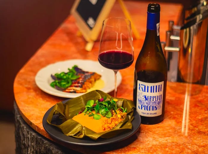 A vibrant yellow tamal garnished with greens, accompanied by a glass of red wine and another dish.